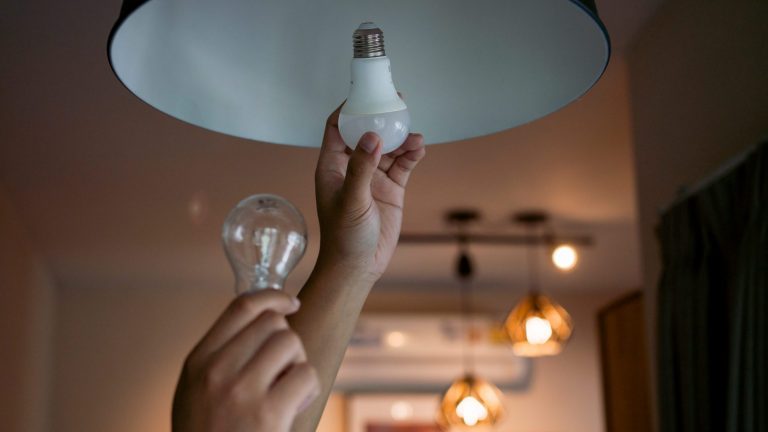 Eine Person entfernt eine klassische Glühlampe aus einer Hängelampe und tauscht sie gegen eine LED-Lampe.