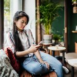 Eine Person sitzt auf einer Holzbank in einem Café und schaut auf ihr Smartphone.