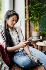 Android: So erstellst du eine Erinnerung Eine Person sitzt auf einer Holzbank in einem Café und schaut auf ihr Smartphone.