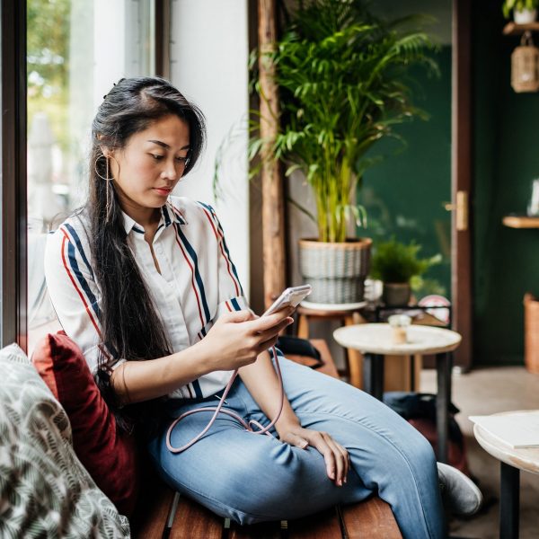 Eine Person sitzt auf einer Holzbank in einem Caf&eacute; und schaut auf ihr Smartphone.