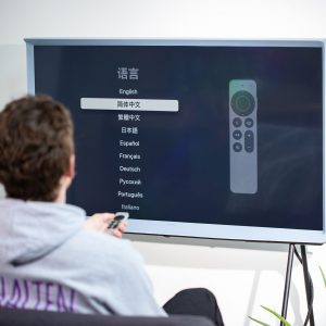 Eine Person sitzt vor einem Fernseher, an den ein Apple TV angeschlossen ist und stellt die Sprache für das System ein.