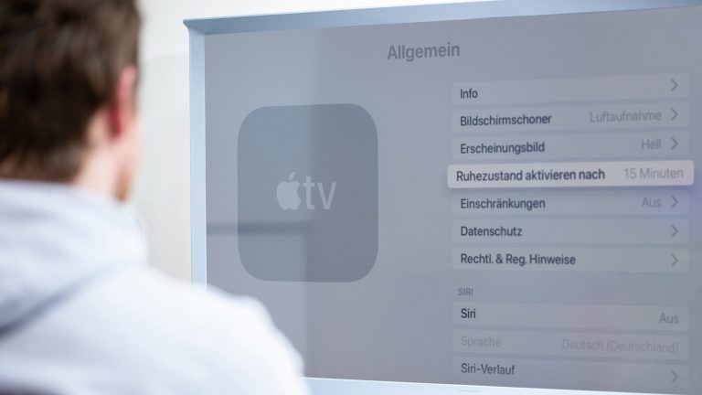 Eine Person sitzt vor einem Fernseher und navigiert durch die Einstellungen eines Apple TV.