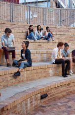 Mehrere Studierende sitzen auf ihrem Campus in Gruppen zusammen.