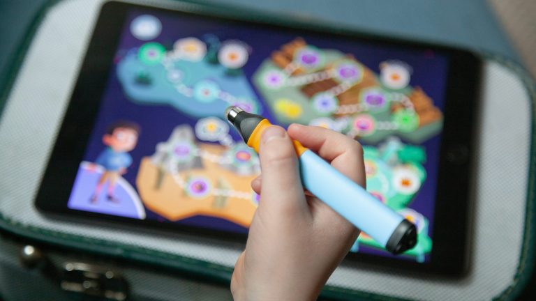 Eine Kinderhand hält einen Edurino-Stift über ein Tablet, auf dem die Edurino-App geöffnet ist.