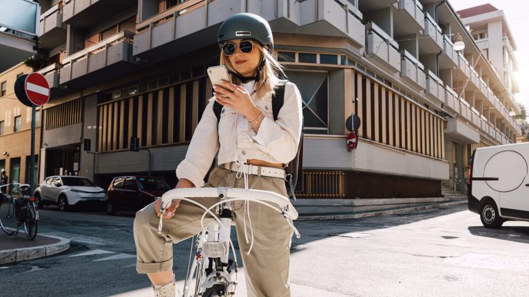 Eine Person steht mit einem Fahrrad auf einer Straße und schaut auf ihr Smartphone.