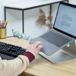 Eine Person sitzt an einem Schreibtisch vor einem Laptop und tippt auf dessen Touchpad.