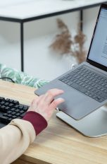 Eine Person sitzt an einem Schreibtisch vor einem Laptop und tippt auf dessen Touchpad.