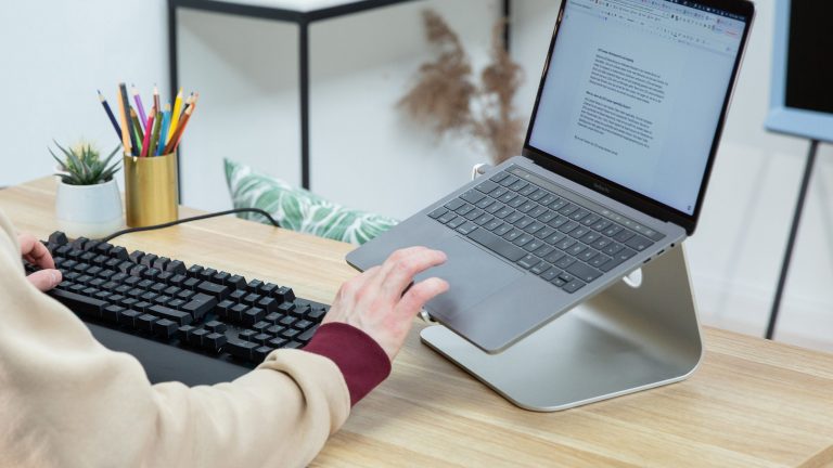 Eine Person sitzt an einem Schreibtisch vor einem Laptop und tippt auf dessen Touchpad.
