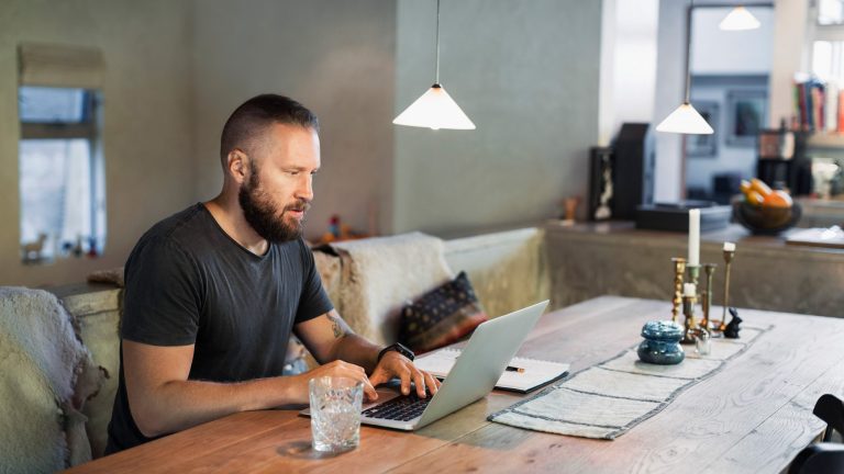 Eine Person sitzt mit ihrem Laptop am Tisch.