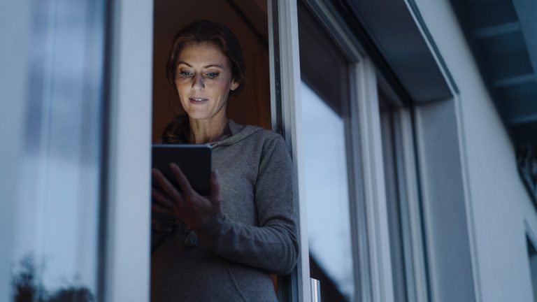 Eine Person steht mit einem Tablet in der Tür zur Terrasse.