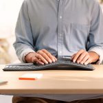 Eine Person sitzt am Schreibtisch und tippt auf einer ergonomischen Tastatur.