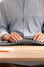 Eine Person sitzt am Schreibtisch und tippt auf einer ergonomischen Tastatur.