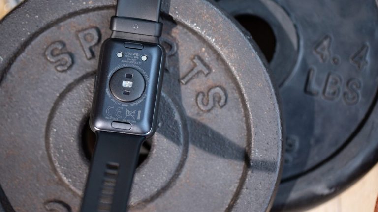 Eine Huawei Watch Fit liegt rückseitig auf einigen Hantelscheiben. Zu erkennen sind die Sensoren des Fitness-Trackers.
