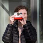 Eine Person richtet blickt durch eine Polaroid Now, die in Richtung Betrachter*in zeigt.