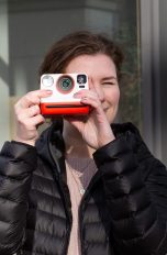 Eine Person richtet blickt durch eine Polaroid Now, die in Richtung Betrachter*in zeigt.