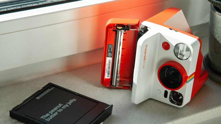 Eine geöffnete Polaroid-Kamera nebst Filmkassette liegen auf einer Fensterbank.