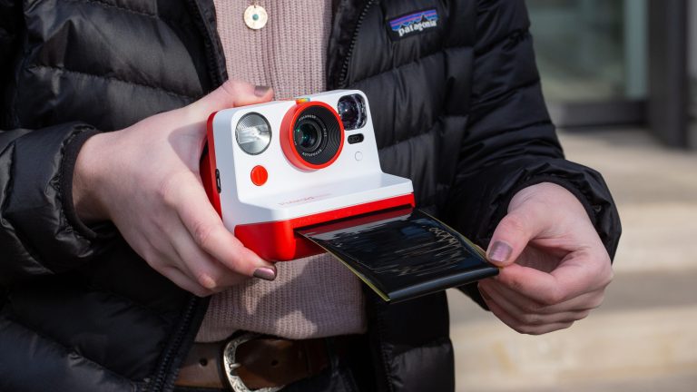 Eine Person hält eine Polaroid-Kamera in den Händen, die gerade ein Foto ausdruckt.