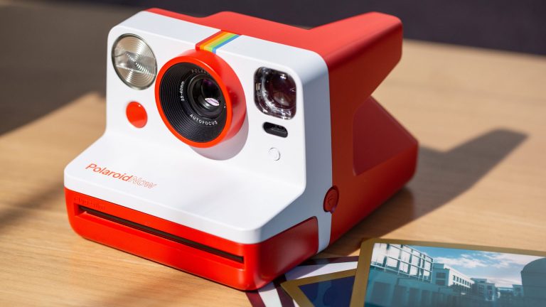 Eine Polaroid-Kamera liegt auf einem Tisch, daneben mehrere Ausdrucke.
