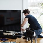 Eine Person kniet auf dem Boden neben ihrem Fernseher und arbeitet an der Verkabelung.