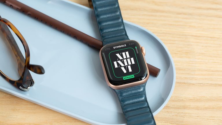 Apple Watch Zifferblätter Eine Apple Smartwatch liegt auf einer Schale aus Kunststoff, unter ihr ein Buntstift, daneben eine Brille.