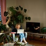 Eine Person sitzt im Wohnzimmer in einem Sessel, mit einem Laptop auf dem Scho&szlig;.
