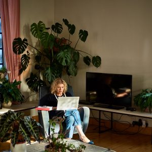 Eine Person sitzt im Wohnzimmer in einem Sessel, mit einem Laptop auf dem Schoß.