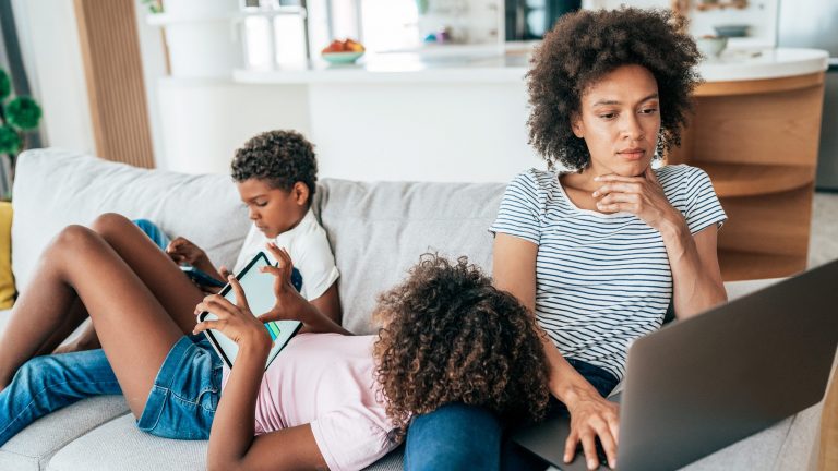 Drei Personen sitzen und liegen auf einem Sofa, sie surfen auf Laptop, Tablet und Smartphone.