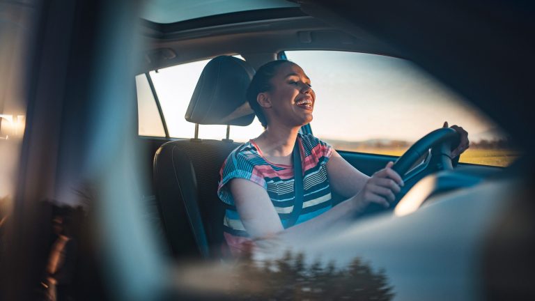 Eine Person sitzt hinter dem Lenkrad ihres PKW und lacht.