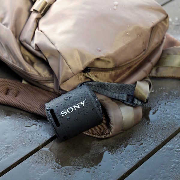Ein schwarzer Sony SRS-XB13 h&auml;ngt an einem nassen Rucksack.