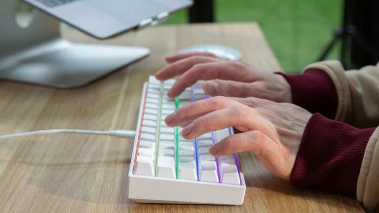 Eine Person tippt auf einer bunt leuchtenden Corsair K65 Mini.