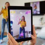 Eine Person h&auml;lt ein Tablet in die Luft. Darauf ist eine junge Person zu sehen, die gerade mit einem &bdquo;Pictionary Air&ldquo;-Stift ein Herz in die Luft zeichnet und von der Kamera des Tablets dabei gefilmt wird.