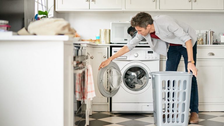Eine Person steht mit einem Wäschekorb vor einer Waschmaschine.