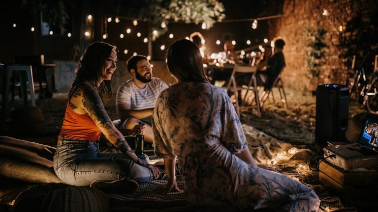 Eine Gruppe Menschen sitzt am Abend in einem Garten mit Lichterketten.