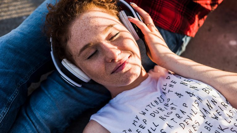 Eine Person trägt einen Kopfhörer und liegt auf einem Kissen.