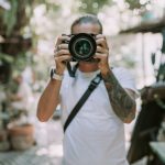 Eine Person hält blickt durch den Sucher einer Kamera mit großem Objektiv, um ein Foto aufzunehmen.