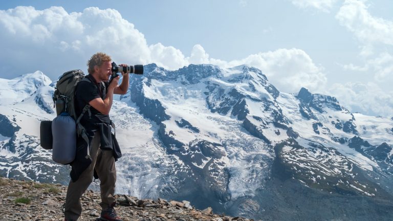 Eine Person steht mit einem Reiseobjektiv vor einem schneebedecktem Berg.