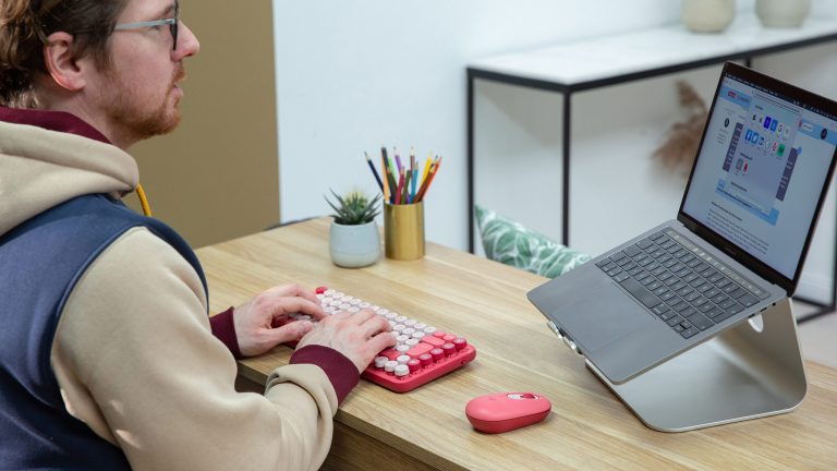 Eine Person tippt auf einer Logitech Pop Keys. Daneben liegen eine farblich passende Maus und ein MacBook Pro.