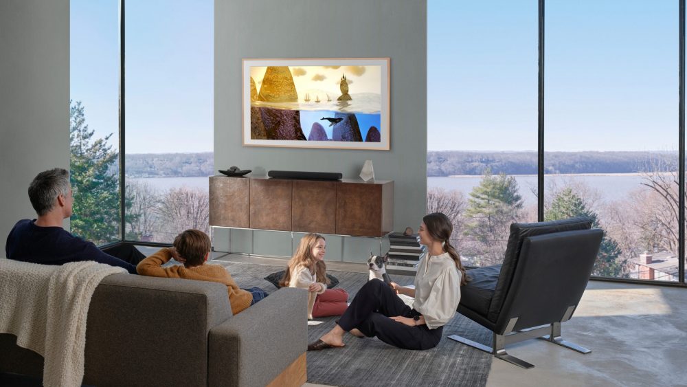 Zwei Eltern sitzen mit ihren beiden Kindern im Wohnzimmer vor einem Fernseher, der an der Wand hängt.