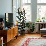 Eine Person steht in einem Wohnzimmer und telefoniert. Auf einer TV-Bank ist ein Fernseher zu sehen.