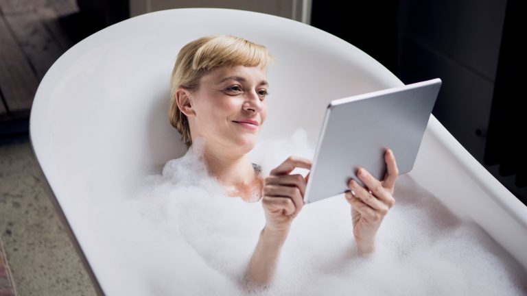 Eine Person in einer Badewanne hält ein Tablet in der Hand.