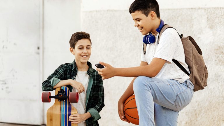 Zwei junge Menschen mit Longboard und Basketball schauen gemeinsam auf ein Smartphone.