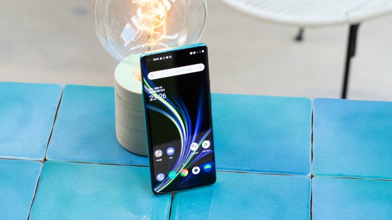 Ein OnePlus 8T steht auf Fliesen angelehnt an eine Lampe.