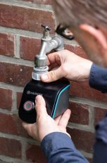 Eine Person bringt einen Bewässerungscomputer an einem Wasserhahn an.