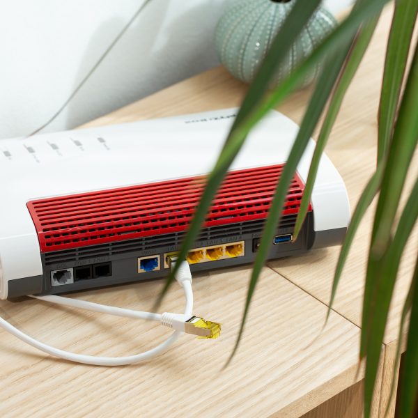 Eine FritzBox steht mit der R&uuml;ckseite zur Kamera auf einem Regal. Es sind zwei LAN-Kabel zu sehen.