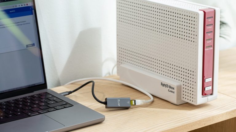 Eine FritzBox Cable steht auf einem Regal. Daneben ist ein angeschlossenes MacBook zu sehen.