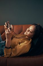 Eine Person liegt auf einem Sofa und spielt dabei auf ihrem Smartphone.