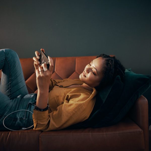 Eine Person liegt auf einem Sofa und spielt dabei auf ihrem Smartphone.