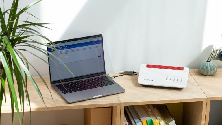Laptop und FritzBox stehen auf einem Regal nebeneinander.
