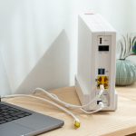 Neben einem Laptop steht ein Router, aus dem ein LAN-Kabel herausf&uuml;hrt.