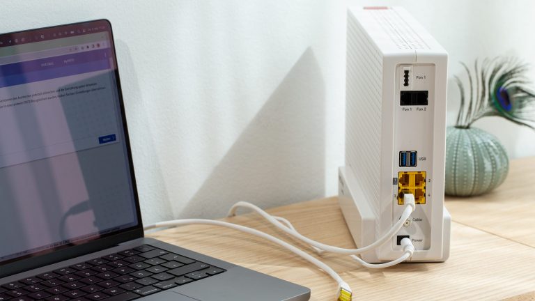 Neben einem Laptop steht ein Router, aus dem ein LAN-Kabel herausführt.